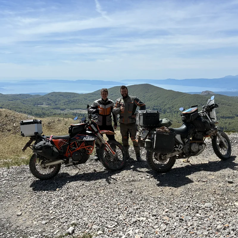 Zwei WildTraX-Fahrer mit Motorrädern vor Berg- und Küstenlandschaft